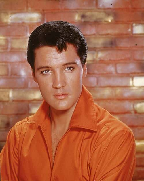 Portrait of American rock and roll singer Elvis Presley, dressed in an orange open-neck shirt and in front of a brick wall, mid 1960s. (Photo by Hulton Archive/Getty Images)