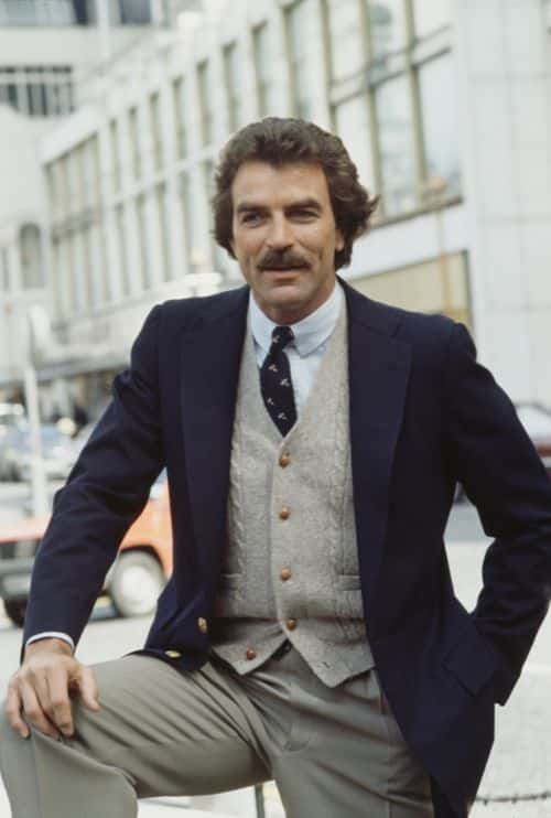 American actor Tom Selleck, wearing a blue blazer over a knitted waistcoat and white shirt with a blue patterned tie, filming his series 'Magnum PI' in London, England, 2nd May 1985. Selleck is filming 'Deja Vu,' an episode of the series in which he plays private investigator Thomas Magnum. (Photo by Keystone/Hulton Archive/Getty Images)