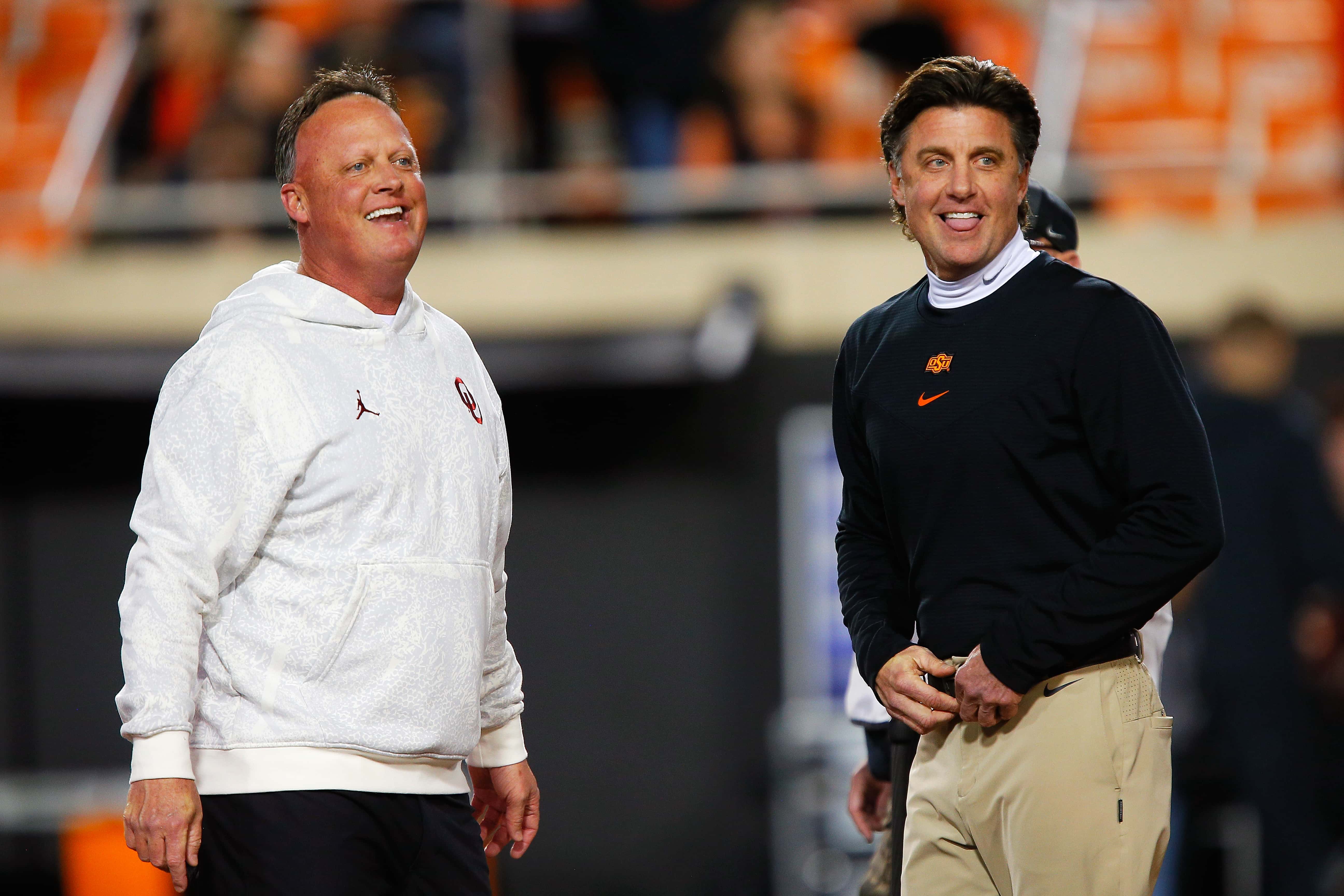 Offensive coordinator Cale Gundy of the Oklahoma Sooners greets his brother, head coach Mike Gundy of the Oklahoma State Cowboys, before their game at Boone Pickens Stadium on November 27, 2021 in Stillwater, Oklahoma.