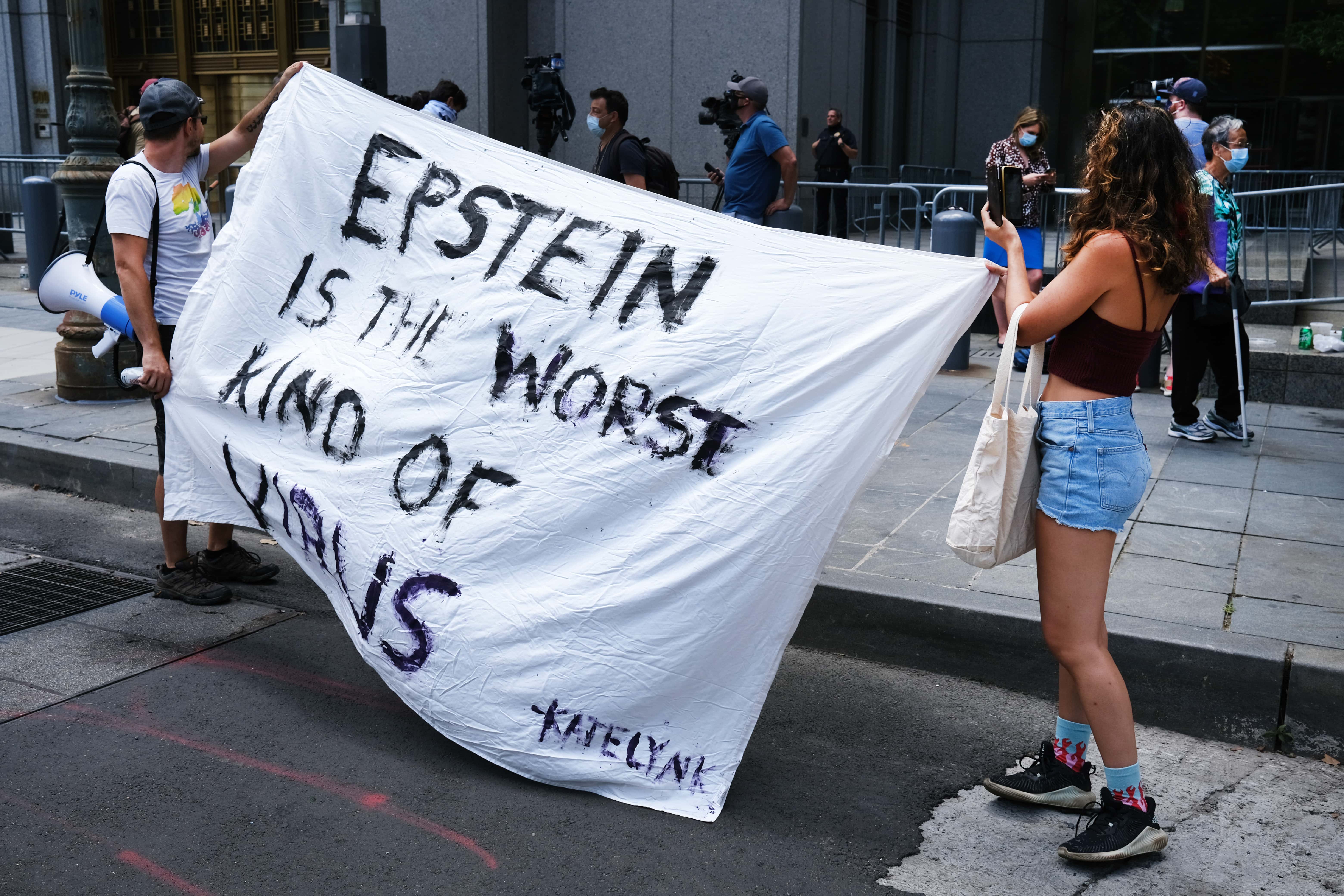 People hold a banner protesting against Jeffrey Epstein while outside a Manhattan courthouse where media has gathered for the arraignment hearing of Ghislaine Maxwell on July 14, 2020 in New York City. Maxwell, the British socialite, longtime girlfriend and alleged accomplice of deceased, accused sex-trafficker Jeffrey Epstein, was recently arrested in New Hampshire and is charged by New York federal prosecutors with six counts in connection with the ongoing federal investigation into Epstein's accomplices. Calling her a flight risk, prosecutors want Maxwell, 58 and who will appear at the hearing via a video link, remanded.