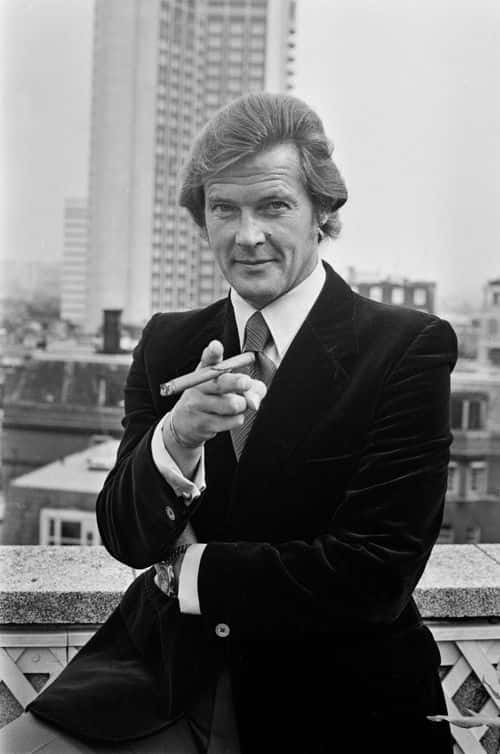 British actor Roger Moore (1927-2017) points towards the camera, a cigar in his hand, at the announcement that 'Live and Let Die' would be the next Bond film, the first to star Moore in the title role, at The Dorchester Hotel in London, England, 2nd August 1972. (Photo by Jack Kay/Daily Express/Hulton Archive/Getty Images)